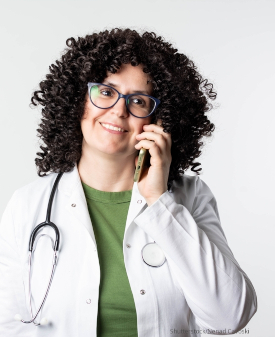 Eine junge Ärztin im weißen Kittel telefoniert mit einem Smartphone.