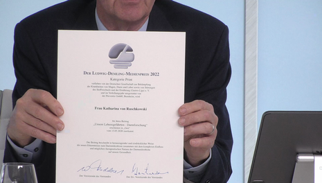 Prof. Fischbach präsentiert die Urkunde des Ludwig-Demling-Medienpreises 2022 in der Kategorie Print.